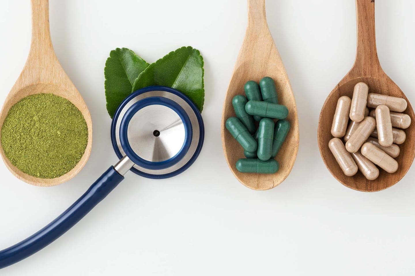 A stethoscope beside wooden spoons of capsules and powdered herbs