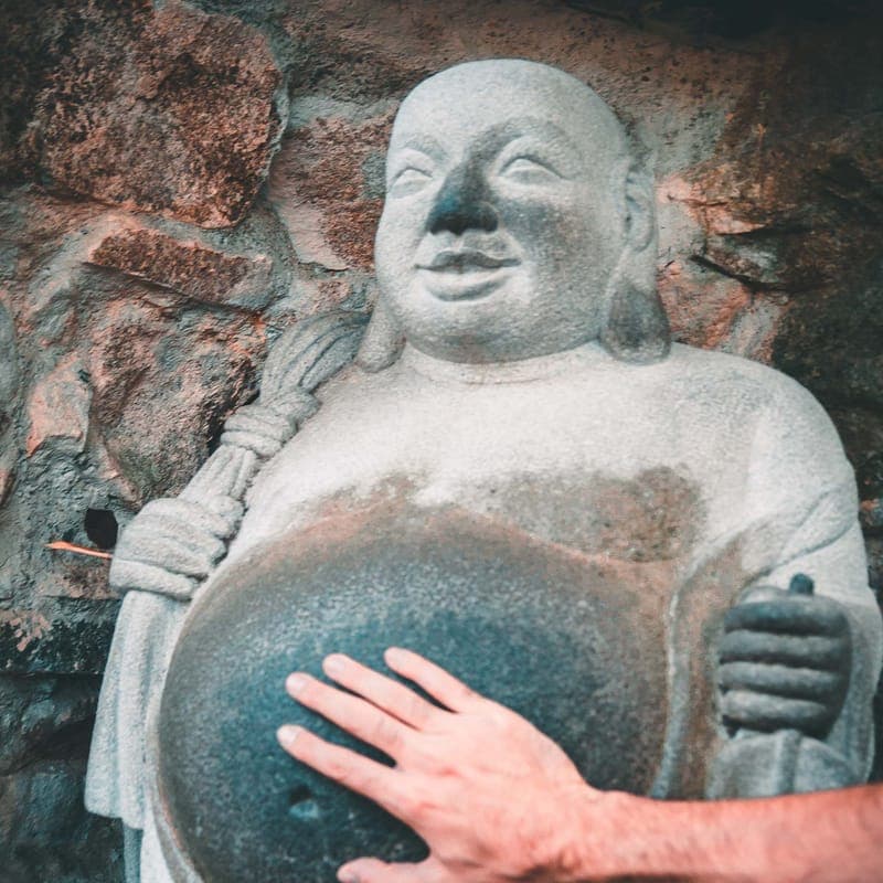 A hand resting on the belly of a carved stone Buddha set into a rock wall.