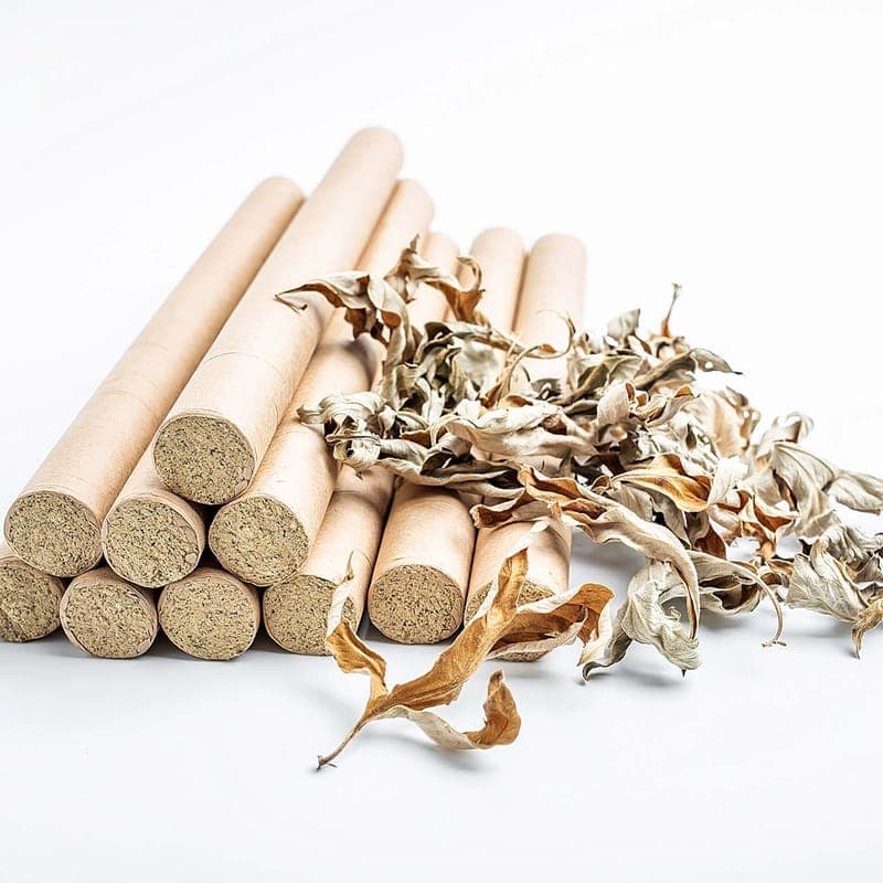 A stack of rolled moxa sticks beside loose dried mugwort leaves.