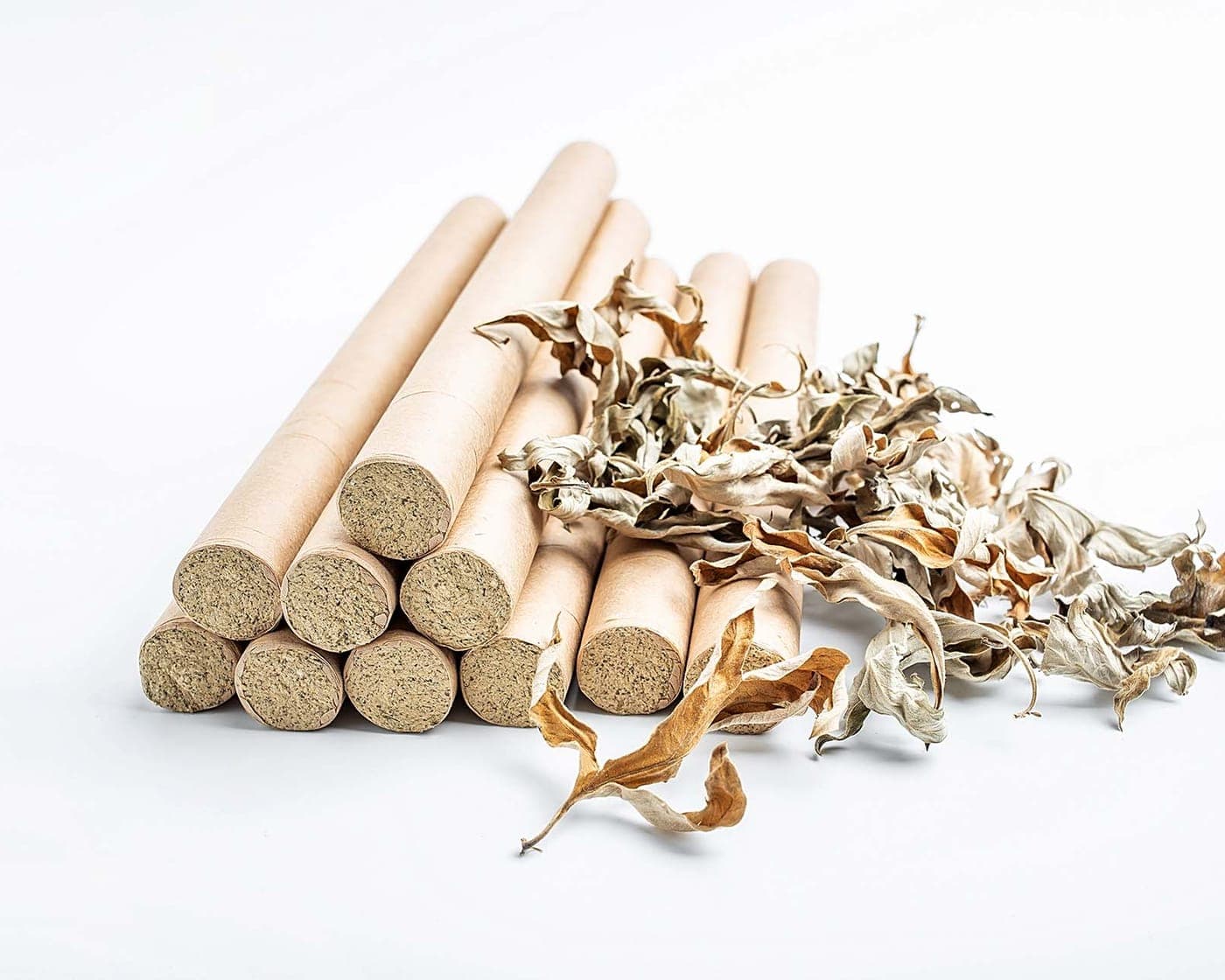 A stack of rolled moxa sticks beside loose dried mugwort leaves.